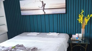 A hotel room with a bed, a desk, a vase with yellow flowers, and a painting of a child jumping with birds. - Flat Frente Mar com Terraço, perto Gran Marquise hotel  e praia (Meireles Fortaleza)