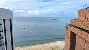 A coastal view with a beach, a large body of water, and a building with a distinctive brick facade. - Flat Frente Mar com Terraço, perto Gran Marquise hotel  e praia (Meireles Fortaleza)