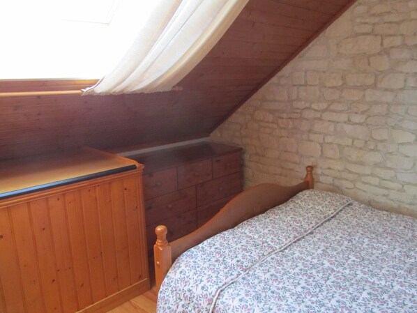Een slaapkamer met een houten bed, een houten dressoir en een stenen muur.