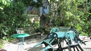 An outdoor seating area with a bench and chairs, surrounded by greenery and potted plants.
