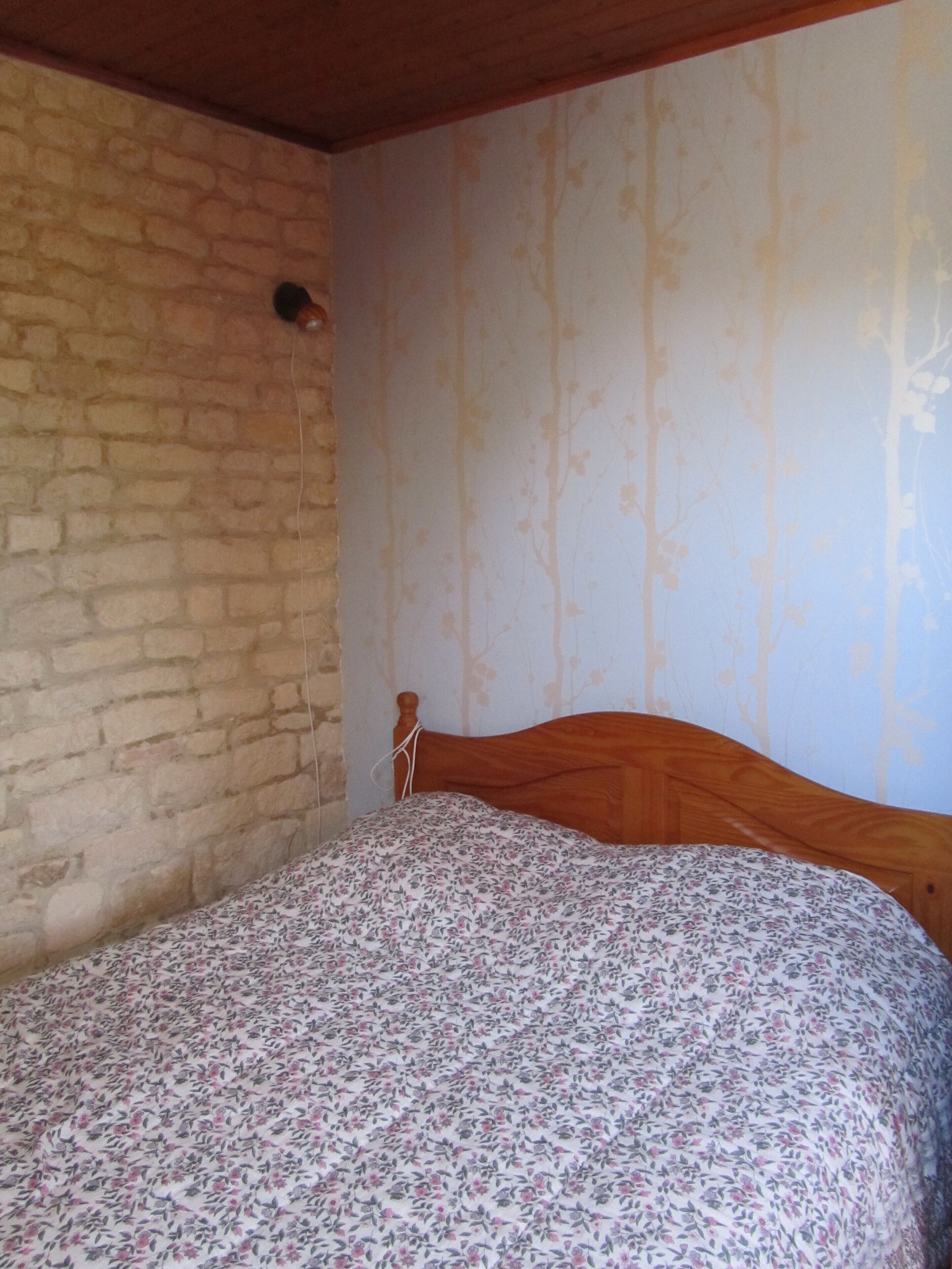 Een slaapkamer met een houten bed, een stenen muur en behang met bloemen.