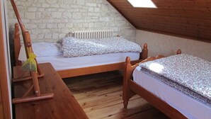 A small, cozy attic bedroom with two wooden beds, a wooden bench, and a stone wall.