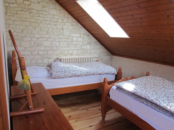 Une petite chambre mansardée, chaleureuse et accueillante, avec deux lits en bois, un banc en bois et un mur en pierre.