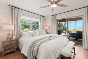 Une chambre à coucher avec un lit, des tables de chevet, un ventilateur de plafond et une vue sur l’extérieur.