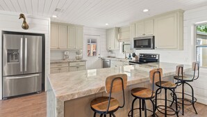 A modern kitchen with a stainless steel refrigerator, a microwave, and a large island with bar stools.