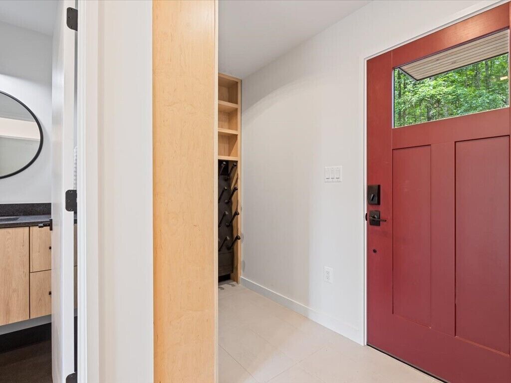 A hallway with a red door, a wooden shelf, and a mirror on the left.