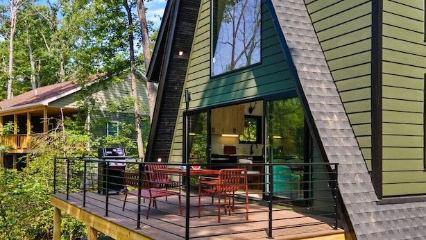 Una cabaña moderna con terraza, jacuzzi y cocina visible a través de amplios ventanales.