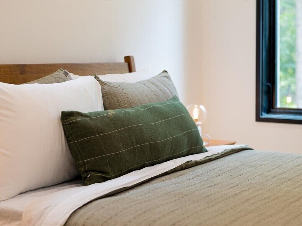 A neatly made bed with a wooden headboard, a green pillow, and a white pillow.