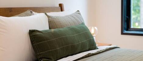 A neatly made bed with a wooden headboard, a green pillow, and a white pillow.