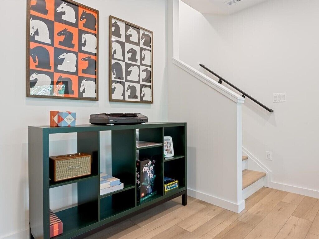 A staircase with a handrail, a green console table with various items, and two framed pictures on the wall.