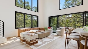 Una sala de estar moderna con ventanas amplias, un conjunto de sofás, una mesa de centro y un comedor con sillas.