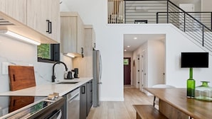 Una cocina moderna con una isla central, electrodomésticos integrados y una escalera que sube a un nivel superior.