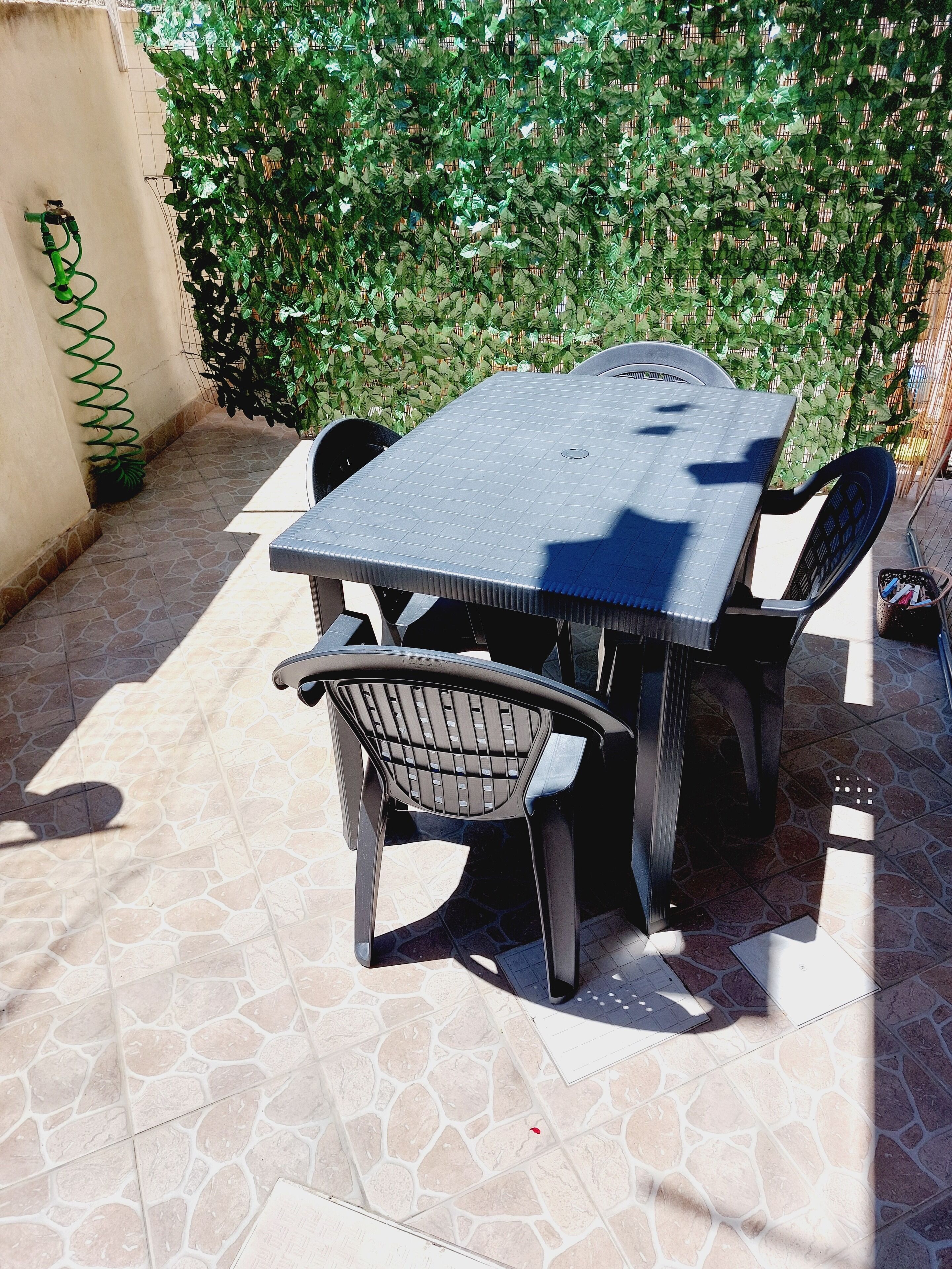 Een terras met een tafel, stoelen, een groene tuinslang en een betegelde vloer.