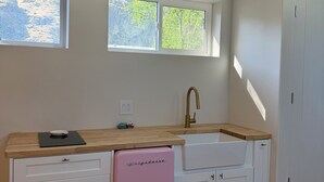 Eine kleine Küche mit Holzarbeitsplatte, Spüle, einem pinken Kühlschrank und einem Fenster mit Blick auf Bäume.