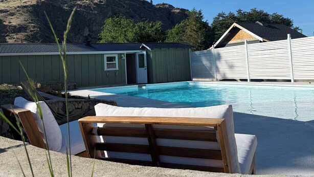 Ein Schwimmbecken mit Liegestühlen, eine kleine Gartenhütte und ein Berg im Hintergrund.