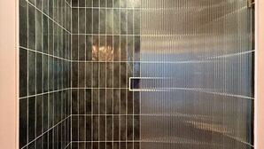 Eine Dusche mit gebogener Glastür und dunkel gefliesten Wänden.