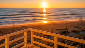 Una spiaggia con ringhiera, onde dell'oceano e un tramonto.