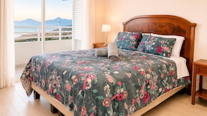 Una camera da letto con un letto, un comodino, una lampada e vista sul mare e sulle montagne dalla finestra.