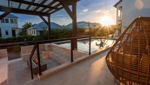 Ein Poolbereich mit einer Pergola, einem Korbstuhl und Blick auf Häuser und Berge im Hintergrund.
