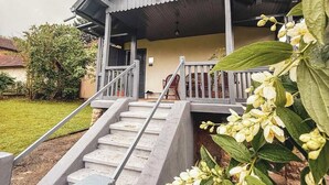 Una casa con porche, una escalera que conduce a la entrada y un jardín con plantas florecientes.