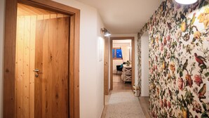 A hallway with a wooden door, a floral wallpaper, and a view into a room with a table and chairs. - Vacation apartment for families and friends with many possibilities. (Fontanella)