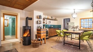A cozy kitchen with a wood-burning stove, a dining area with chairs, and a view of the outside through a window. - Vacation apartment for families and friends with many possibilities. (Fontanella)