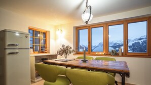 A kitchen with a wooden table, green chairs, a vintage refrigerator, and a window with a mountain view. - Vacation apartment for families and friends with many possibilities. (Fontanella)