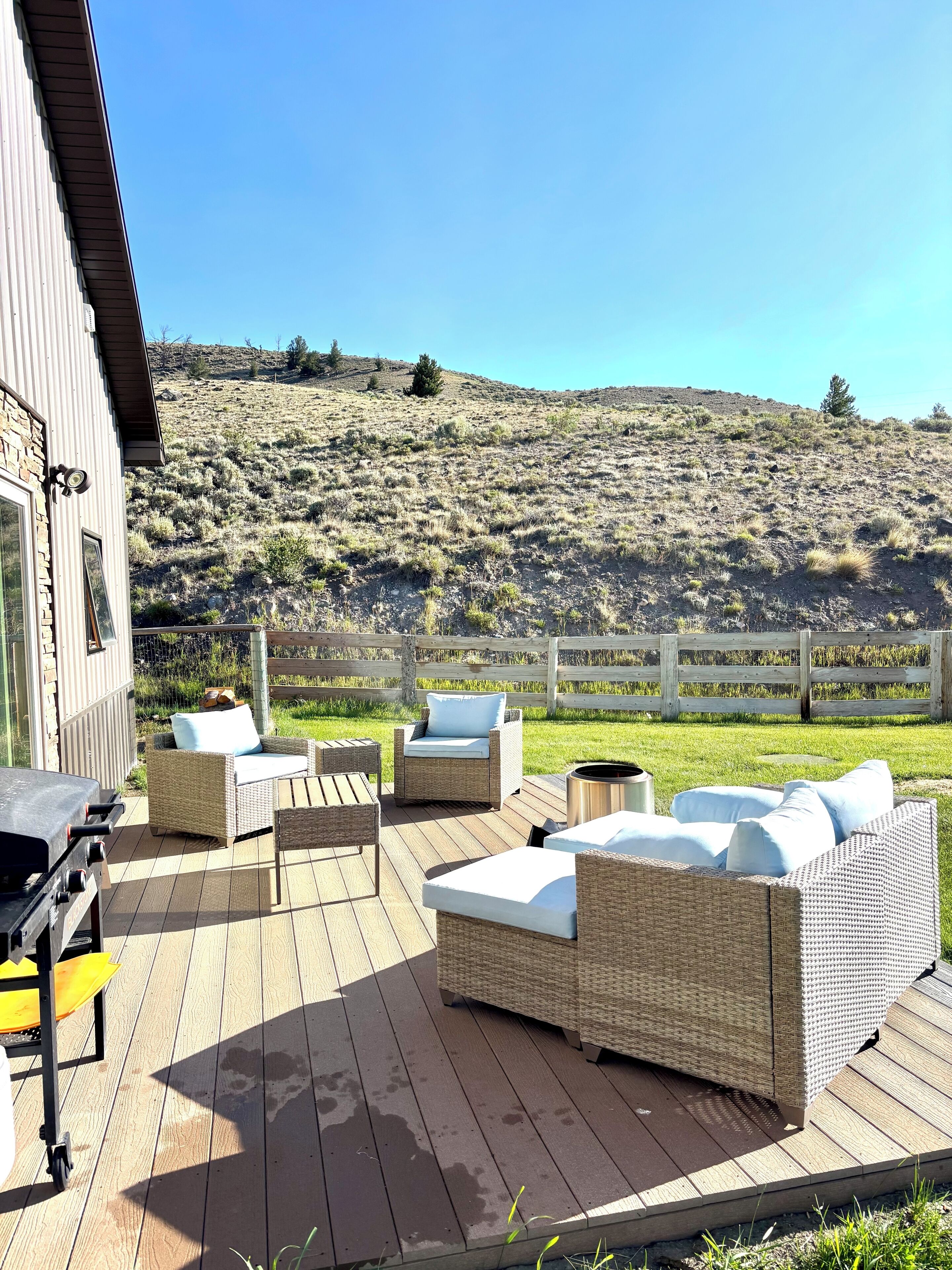 A deck with wicker furniture and a grill, overlooking a grassy hillside.