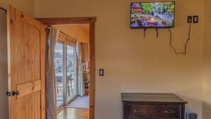 A room with a wooden door, a television mounted on the wall, and a small cabinet. - Near Yellowstone Lucky Dog Ranch, 3BR, Sleeps 8, Full Kitchen, Right off the Hwy (Dubois)
