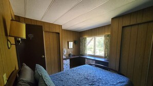 A bedroom with a bed, a desk, a lamp, and a window with curtains.