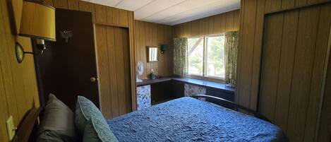 A bedroom with a bed, a desk, a lamp, and a window with curtains.