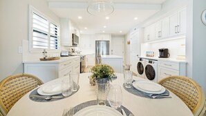 Een moderne keuken met witte kasten, een roestvrijstalen koelkast en een eethoek met een ronde tafel gedekt voor twee personen.