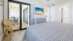 Een slaapkamer met een bed, een stoel, een dressoir en een deur naar een balkon.
