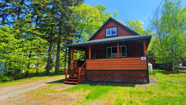 Une cabane en bois dotée d’un porche et d’un petit escalier, entourée d’une végétation luxuriante.