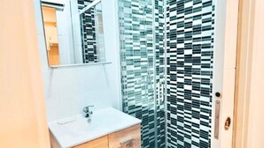 Un baño moderno con tocador blanco, un espejo y una ducha con puerta de vidrio estampado.