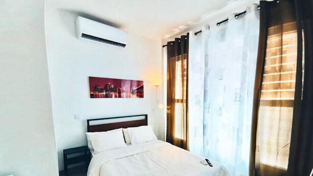 Una habitación de hotel con una cama, aire acondicionado, un cuadro y cortinas.
