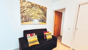 Un sofá negro con cojines a rayas en una habitación con una puerta blanca y un cuadro de árboles en la pared.