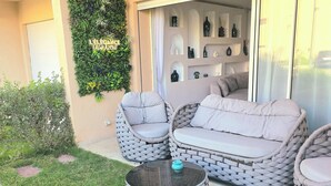 Un espace extérieur aménagé avec des meubles en osier et une table en verre, situé à côté d’un bâtiment doté d’un mur décoratif et d’une porte-fenêtre coulissante.