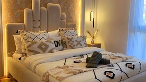 Une chambre à coucher moderne avec une tête de lit au design original, un lit bien fait avec une literie à motifs et un plancher en bois.