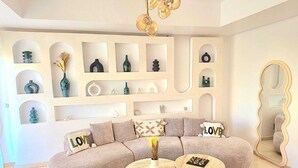 Un salon moderne avec un canapé d’angle, deux petites tables rondes et des étagères décoratives où sont exposés divers objets.