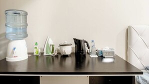 A kitchen counter with a water dispenser, a kettle, a coffee maker, a bottle of water, a bottle of dish soap, and a clock.