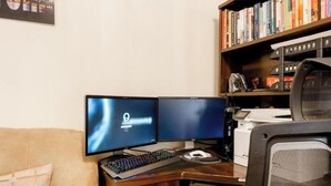 A dual-monitor setup on a desk with a keyboard and mouse, a bookshelf with books, and a chair.