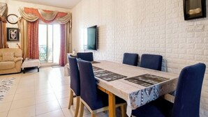 A dining area with a brick wall, a television mounted on the wall, and a sofa in the background.