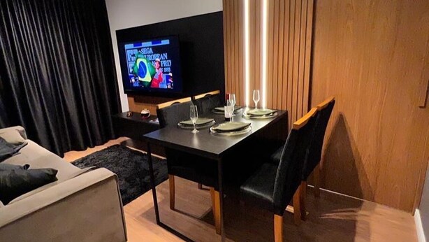 A modern living room with a dining area, a flat-screen TV, and a wooden partition. - Interlagos Autodrome Apartment (Vila da Paz São Paulo)