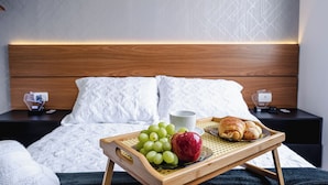 A neatly made bed with a wooden headboard, a bedside table with a cup and a charger, and a tray with grapes, an apple, and a croissant. - Interlagos Autodrome Apartment (Vila da Paz São Paulo)