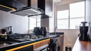 A modern kitchen with a built-in oven, microwave, and coffee maker, featuring a black countertop and wooden accents. - Interlagos Autodrome Apartment (Vila da Paz São Paulo)
