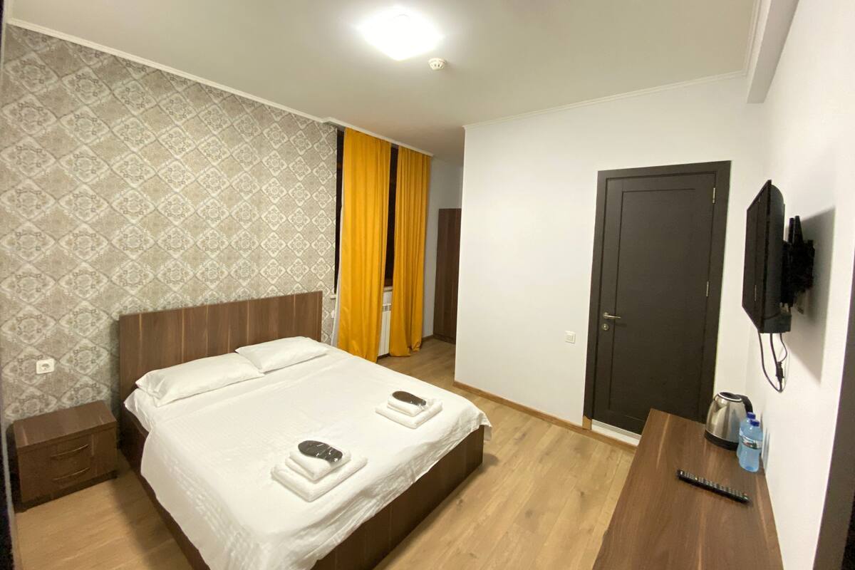 A hotel room with a bed, a TV mounted on the wall, and a door.