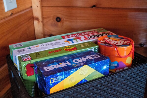 Un bac de rangement contenant divers jeux de société, notamment Monopoly, Scrabble et Catan.