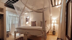 Un dormitorio con cama con dosel, una mesita de noche, una lámpara y una alfombra estampada.