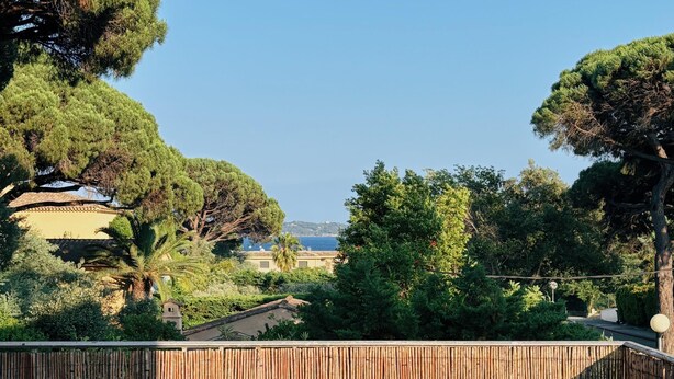 Un espace de restauration en plein air avec une table dressée pour quatre personnes, offrant une vue panoramique sur un paysage verdoyant, avec des arbres et la mer à l'horizon.